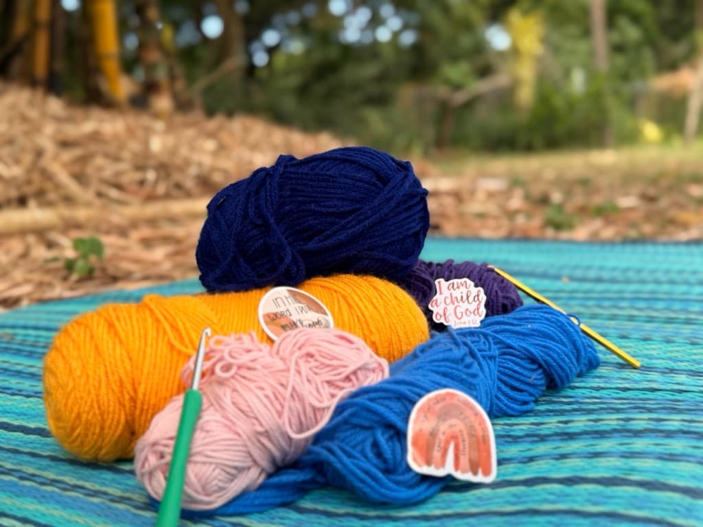 Colorful yarn skeins and crochet hooks arranged on a woven mat outdoors